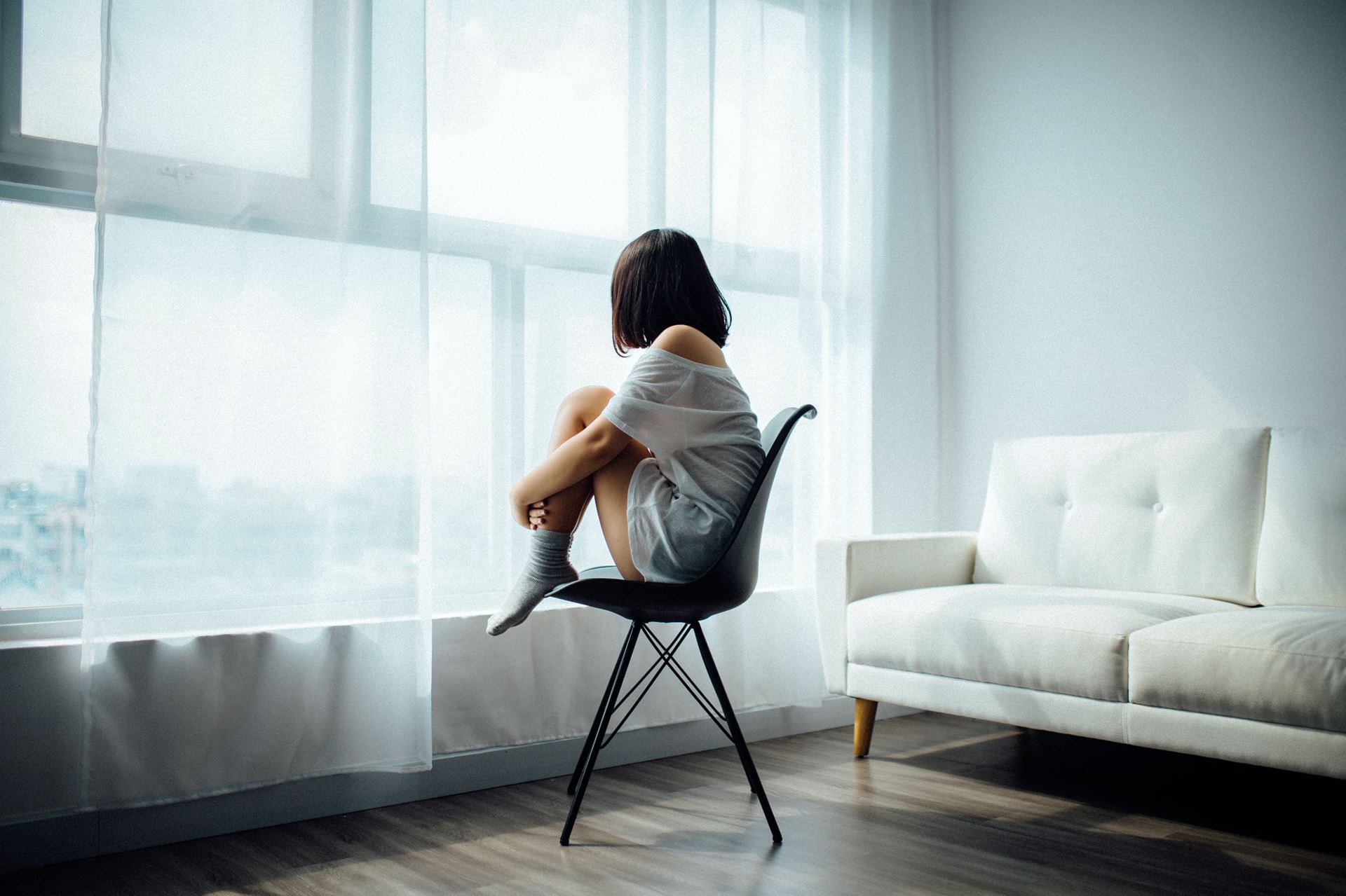 a woman curled up in a chair facing a window her back to the camera
